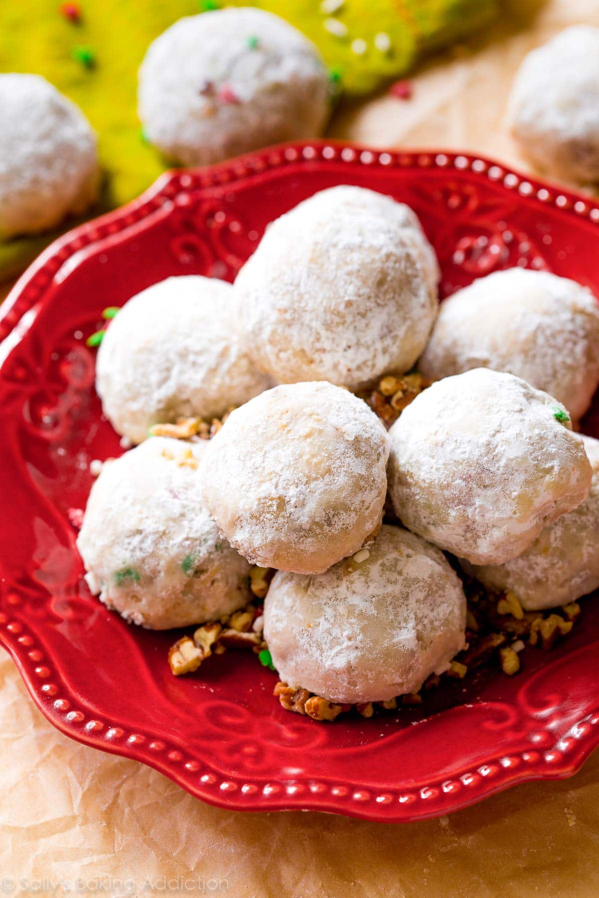 A pile of pecan snowball cookies on a red plate.