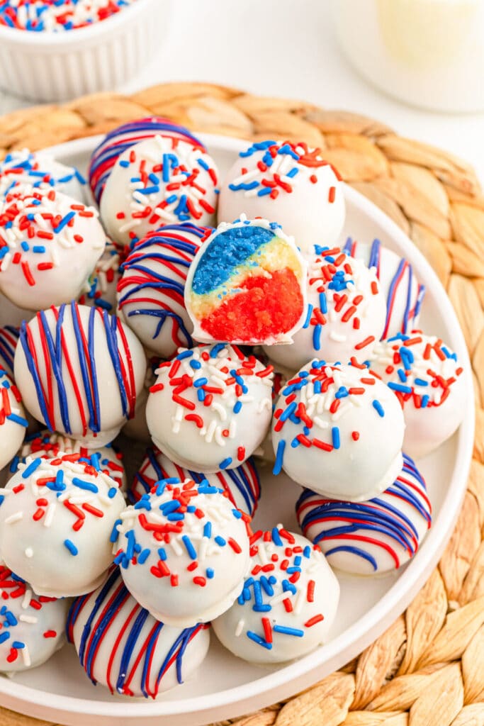 A pile of red white and blue cake balls dipped in white chocolate and topped with sprinkles. 