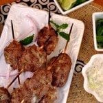 Above view of lamb kebabs on a white square plate.