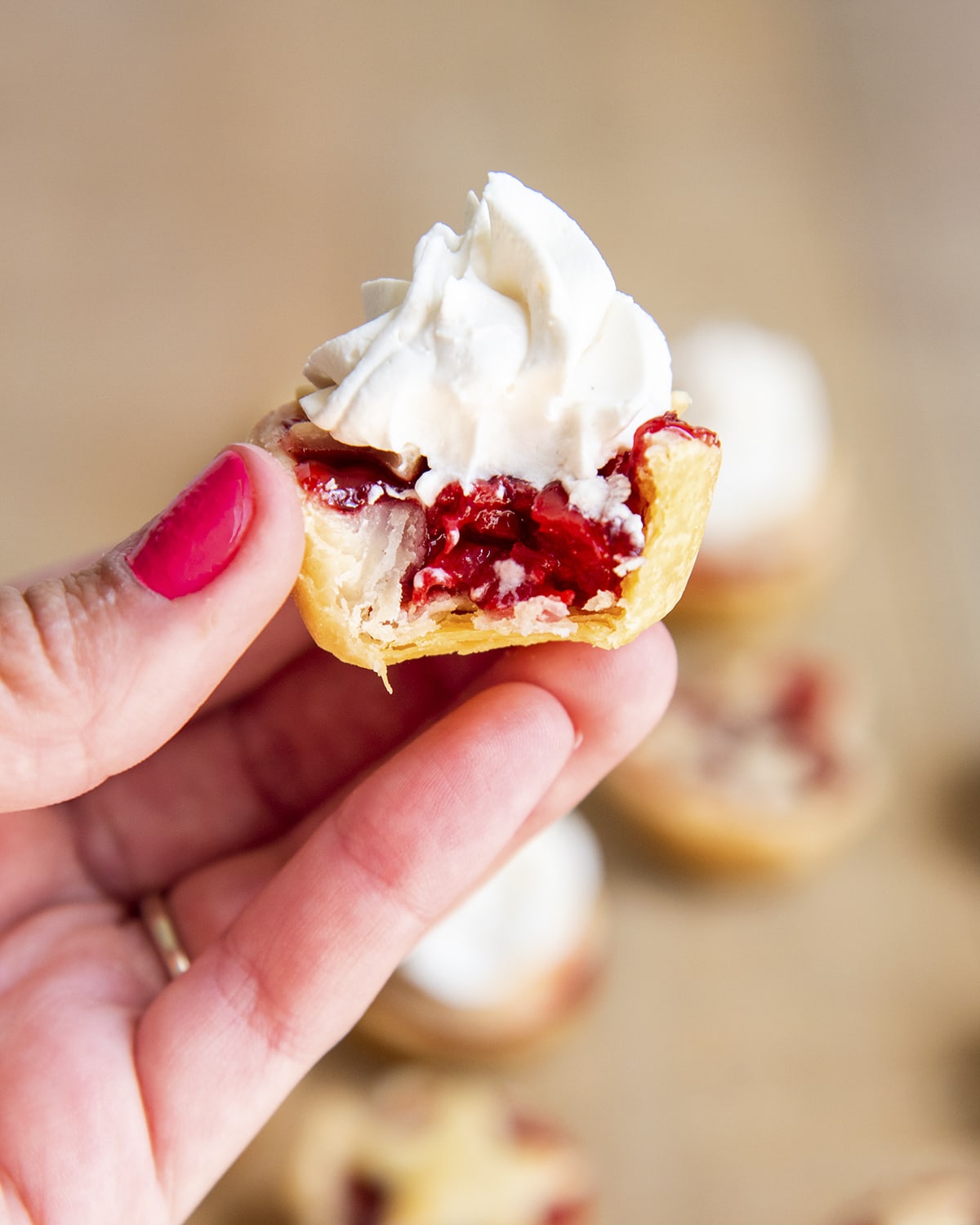 A hand holding a mini cherry pie with a bite out of it, showing the middle.