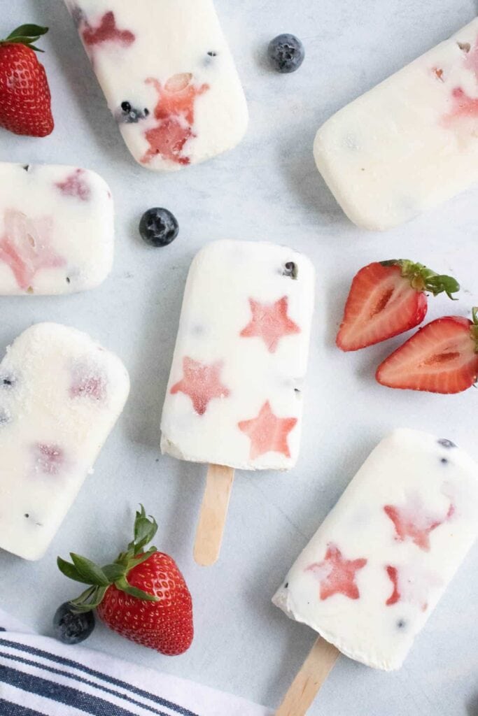 An overhead view of white popsicles loaded with star shaped strawberries and blueberries. 