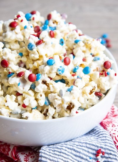 White Chocolate covered Popcorn with red white and blue m&ms and sprinkles in a white bowl