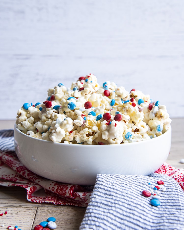 White Chocolate Popcorn with red white and blue m&ms and sprinkles in a white bowl