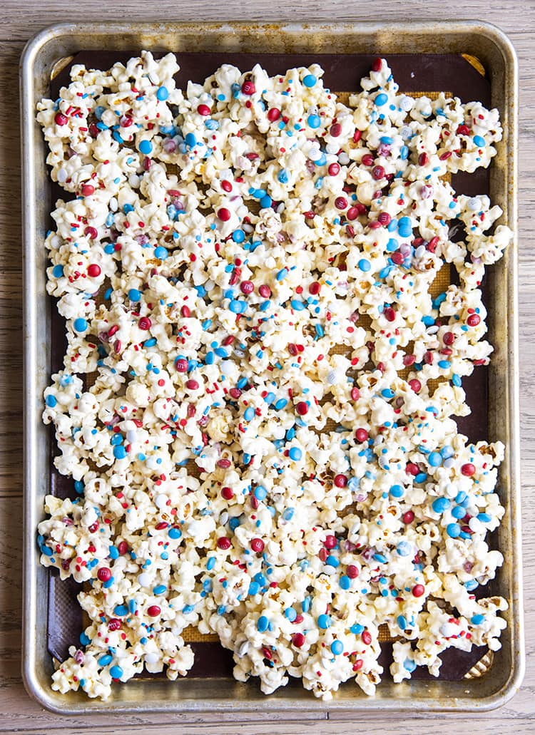 popcorn covered in white chocolate and red white and blue sprinkles and m&ms on a baking tray