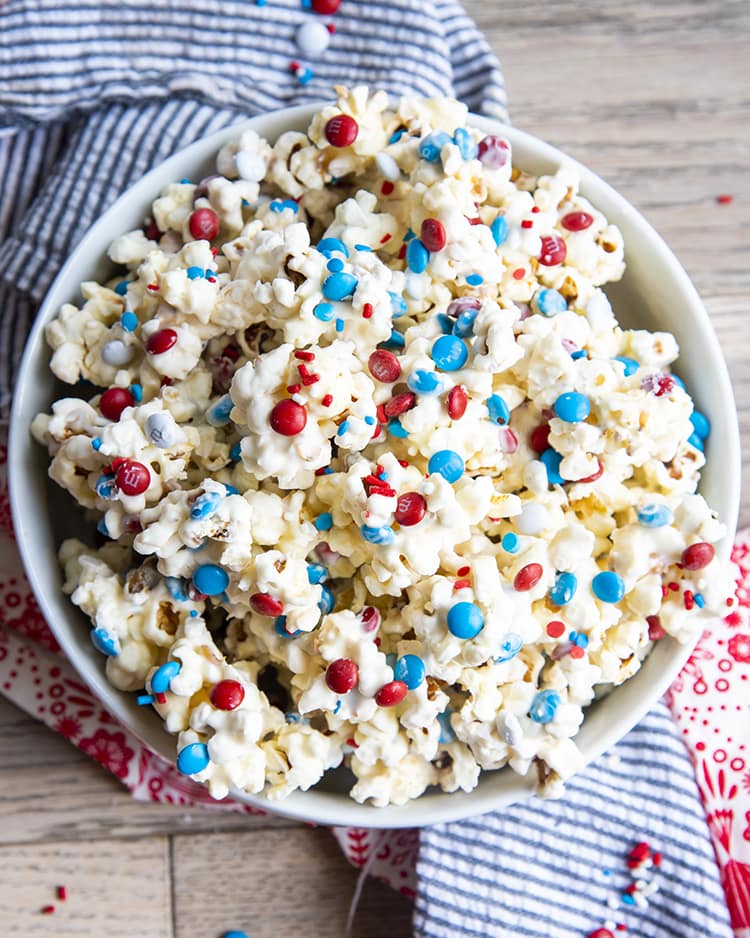 An overhead shot of white Chocolate Popcorn with red white and blue m&ms and sprinkles in a white bowl