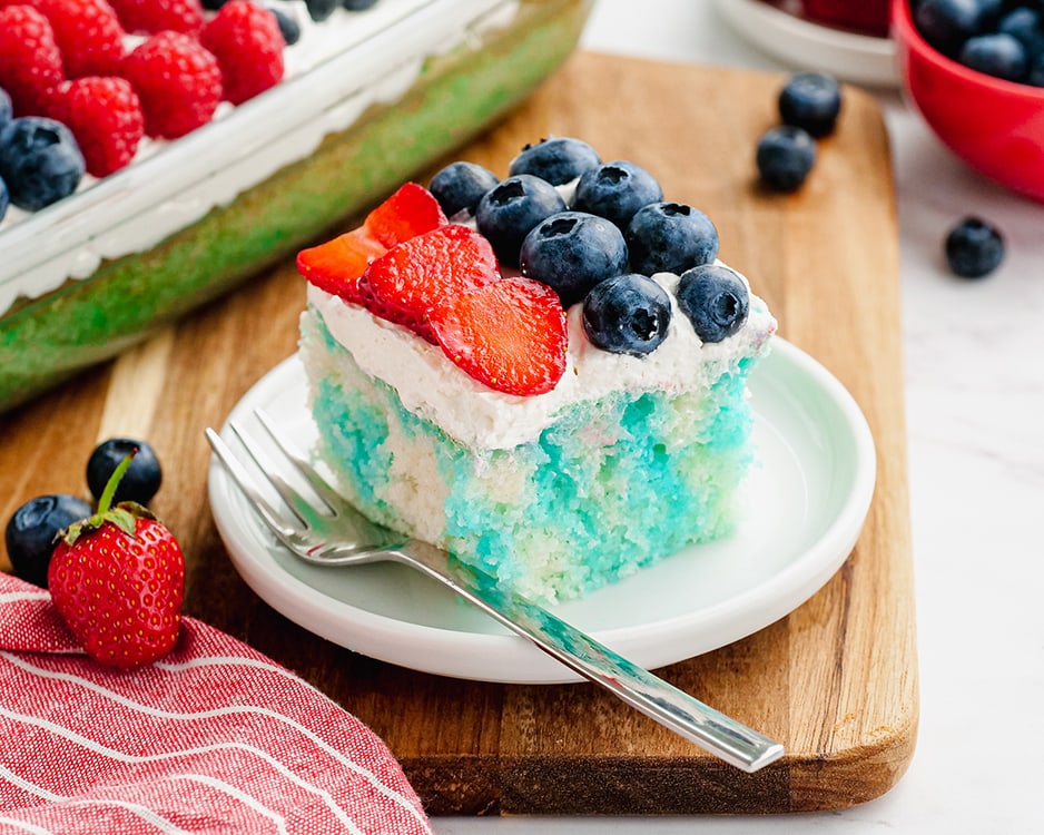 Red White and Blue Jello Poke Cake topped with red strawberries and blueberries and whipped cream