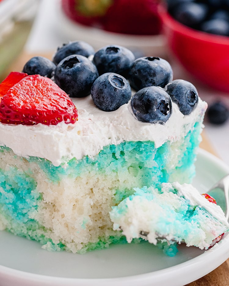Red White and Blue Jello Poke Cake topped with red strawberries and blueberries and whipped cream with a piece on a fork