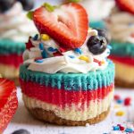 A mini cheesecake with layers of white, red, and blue topped with whipped cream and a fresh strawberry.