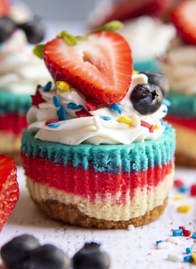 A mini cheesecake with layers of white, red, and blue topped with whipped cream and a fresh strawberry.