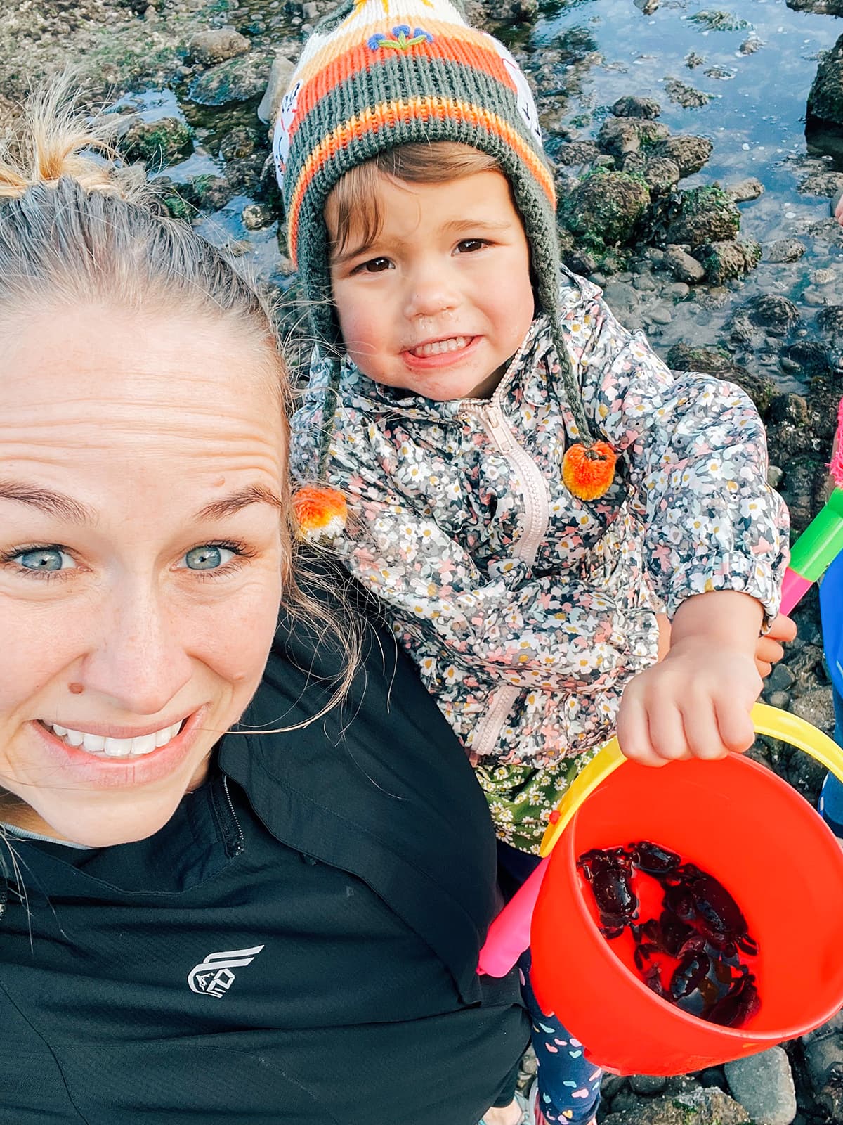 A woman and a little girl holding a bucket with small crabs in it.
