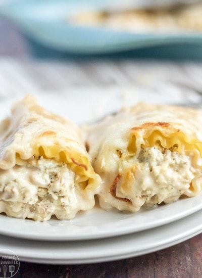 Side image of two chicken alfredo lasagna roll ups on a white plate with filling visible.