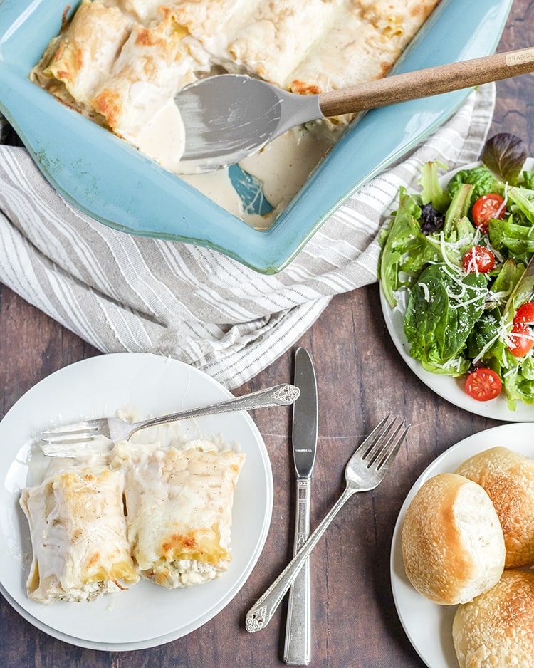 Above image of chicken lasagna roll ups with side salad and rolls.