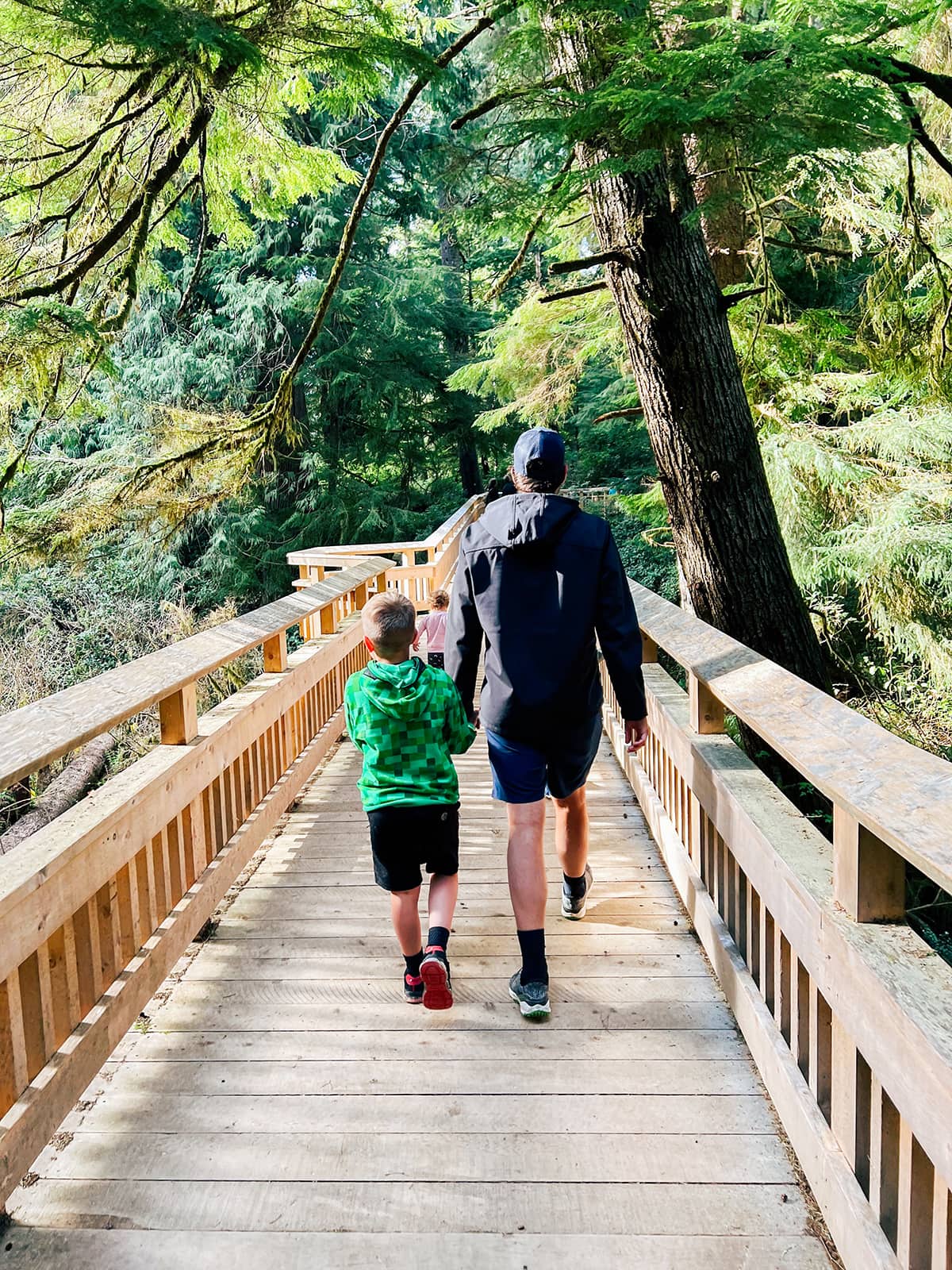 A man and a boy walking on a wooden boardwalk among greenery. 