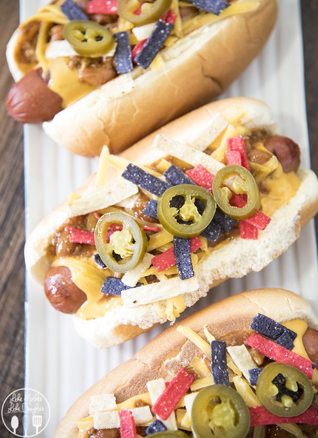 An overhead photo of hot dogs in a bun topped with nacho cheese sauce, tortilla strips, and jalapenos. 