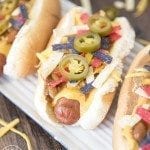 Angled view of nacho hot dogs on a white plate.