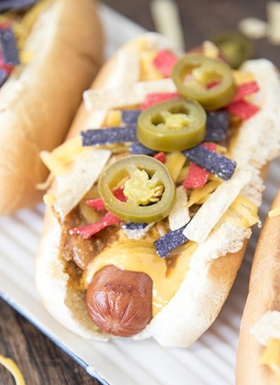 Angled view of nacho hot dogs on a white plate.