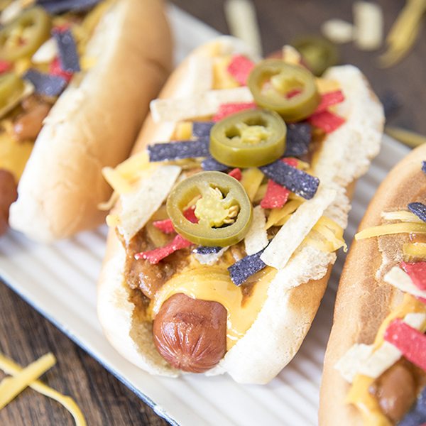 Angled view of nacho hot dogs on a white plate.