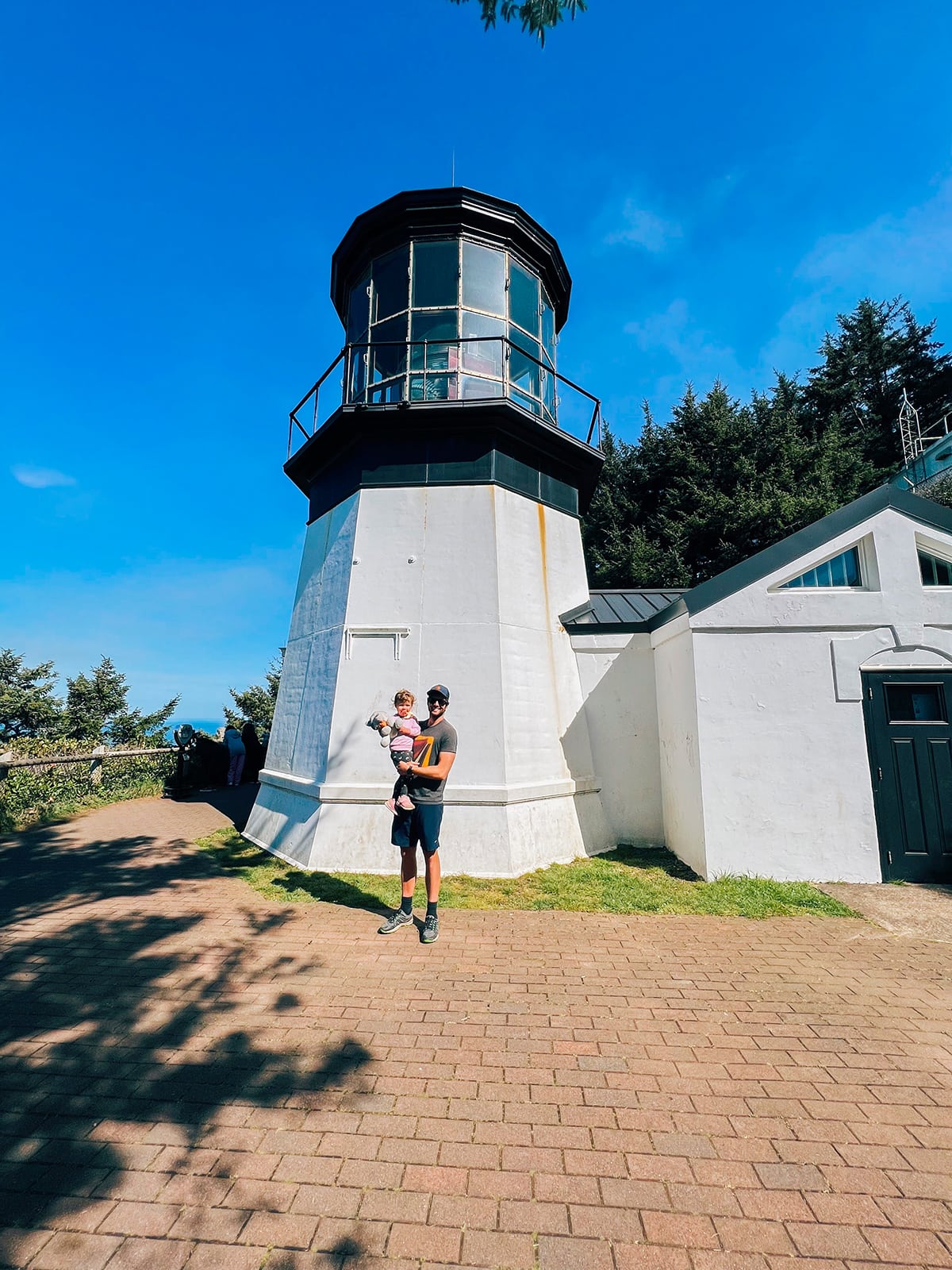A man and baby in front of a white lighthouse. 
