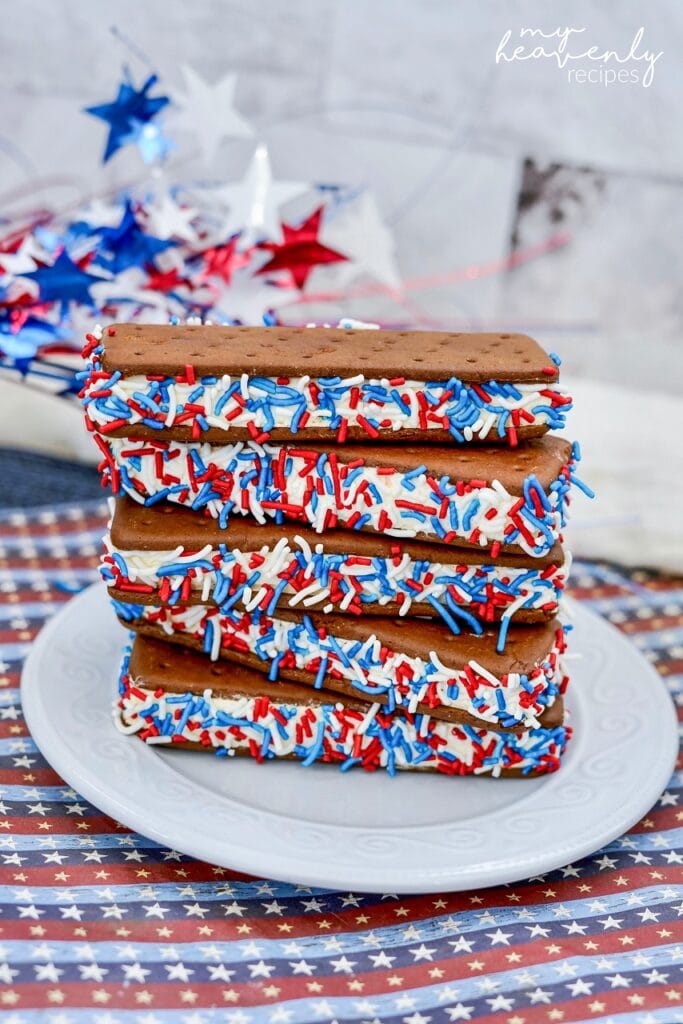 A stack of ice cream sandwiches coated in red white and blue sprinkles on a plate. 