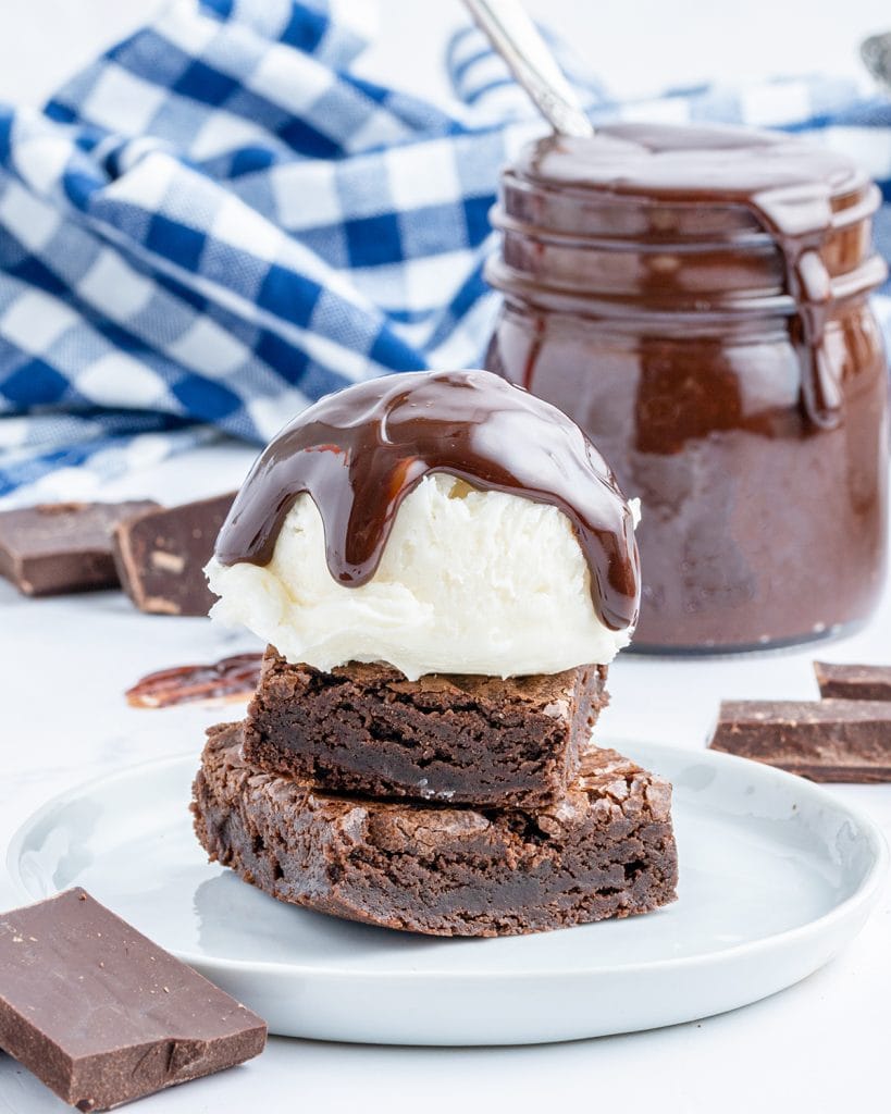 A stack of two brownies topped with a scoop of vanilla ice cream, and hot fudge sauce on top.
