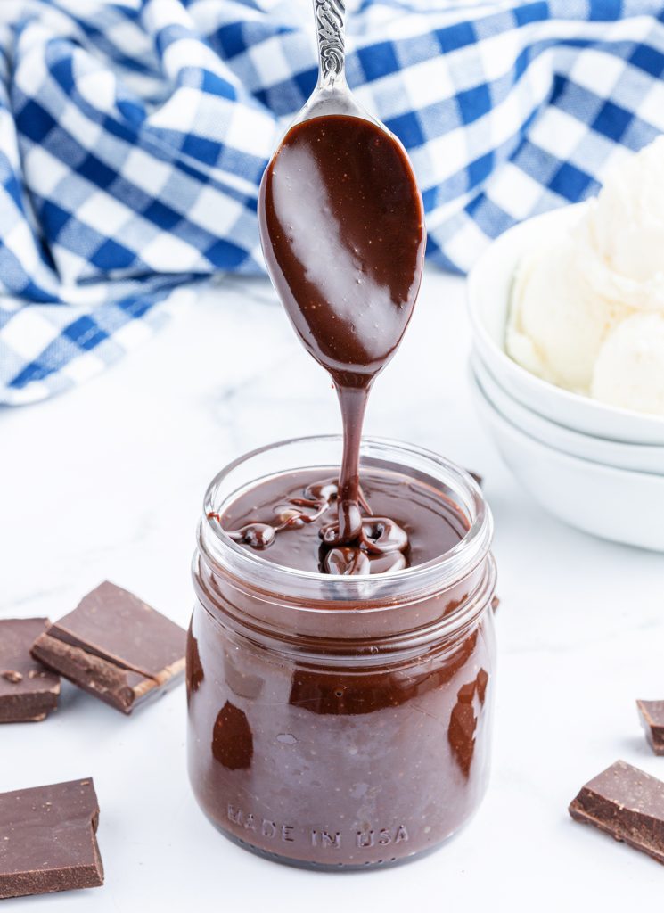 A spoon of hot fudge sauce, drizzling it into a jar of the sauce.