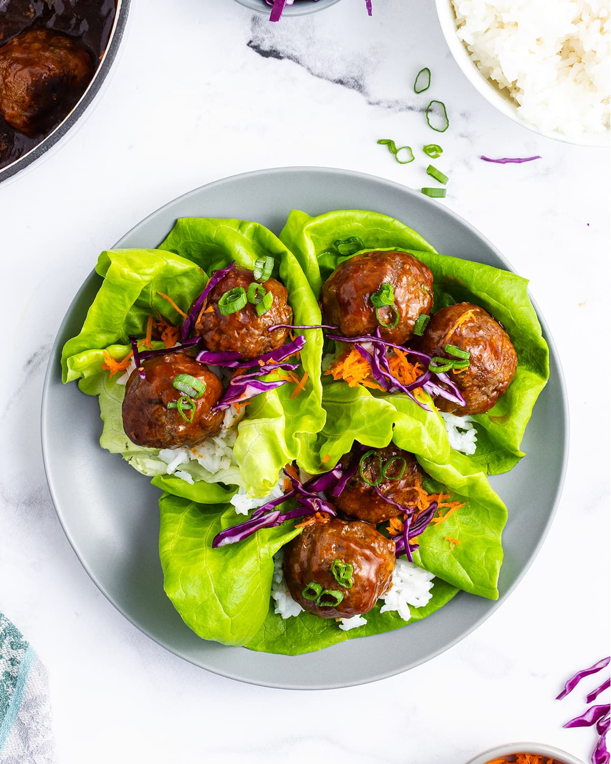 An overhead photo of three lettuce wraps full of white rice and two teriyaki meatballs.
