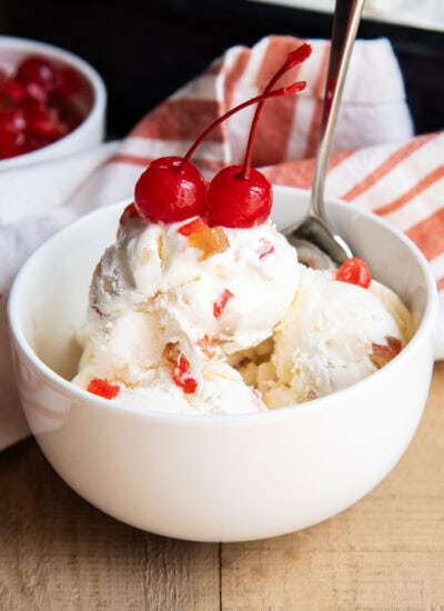 A bowl of ice cream full of candied lemon peels, and topped with two maraschino cherries.