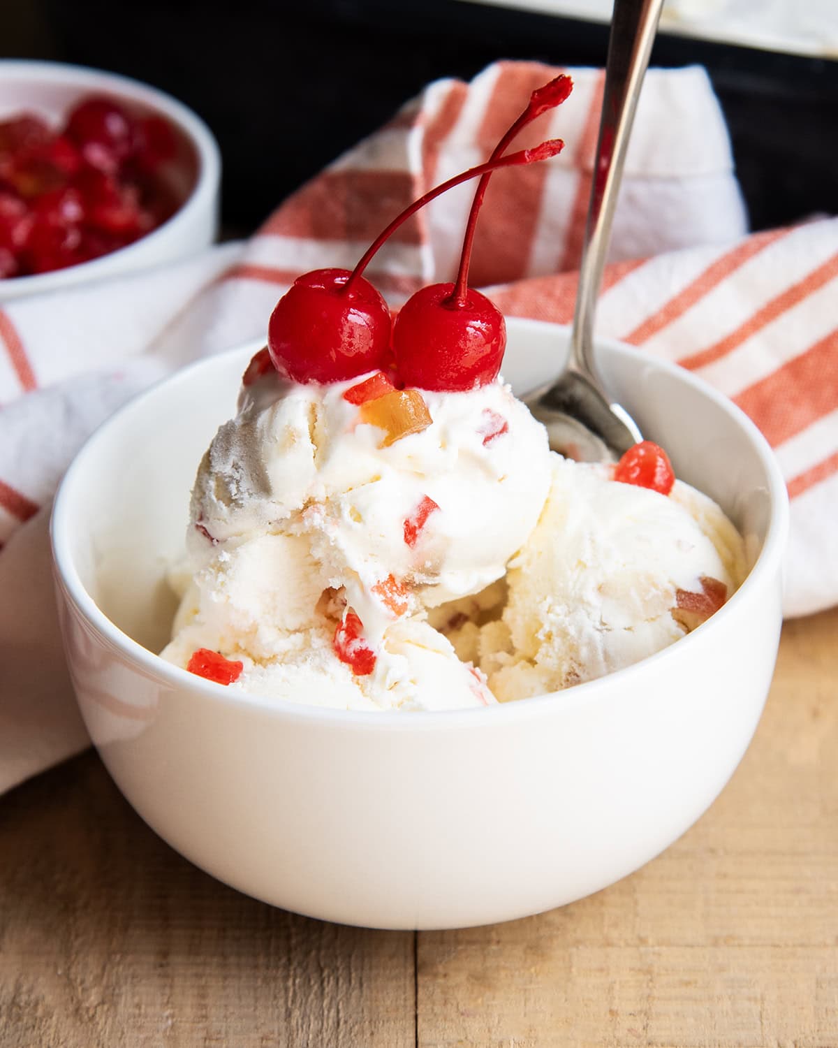A bowl of ice cream full of candied lemon peels, and topped with two maraschino cherries.