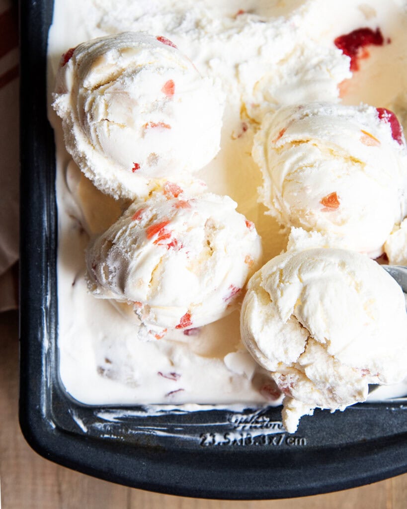 A metal container of tutti frutti ice cream, with scoops of the ice cream on top.