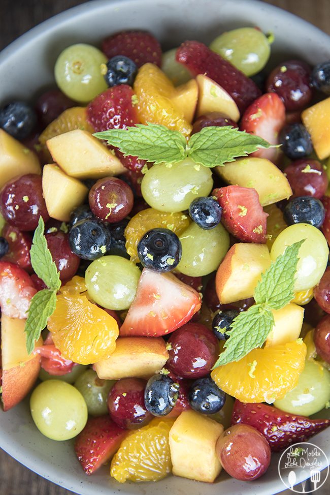 A colorful rainbow fruit salad topped with lime zest, and there are mint leaves around it.