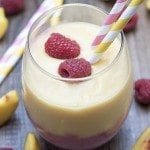 Angled view of raspberry peach smoothie in a glass with straws and raspberries.