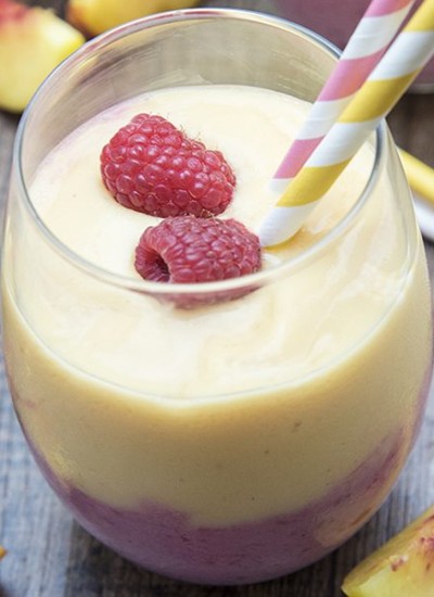 Above view of raspberry peach smoothie in a glass with straws and raspberries.