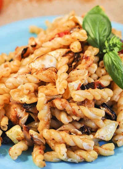 Side view of pasta with roasted summer vegetables on a blue plate.