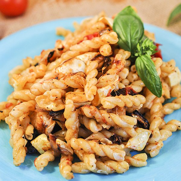 Side view of pasta with roasted summer vegetables on a blue plate.