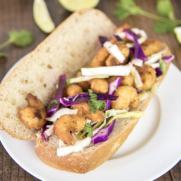 Angled view of shrimp sandwich with cilantro lime cabbage slaw on a plate.
