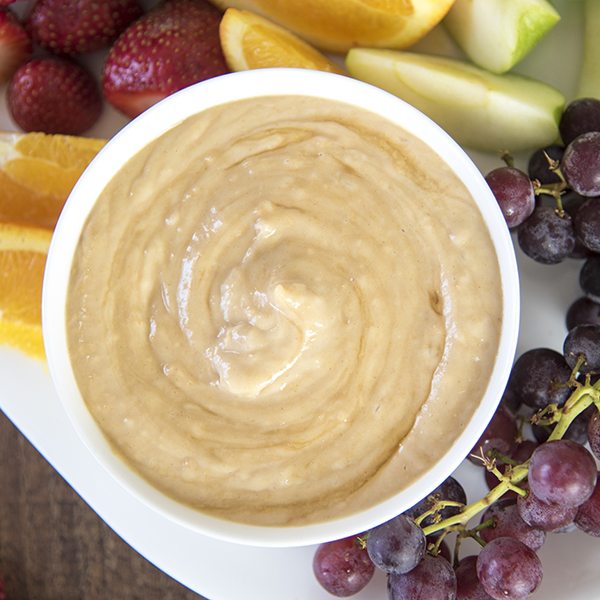 Above view of honey peanut butter yogurt dip in a white bowl with fruit.