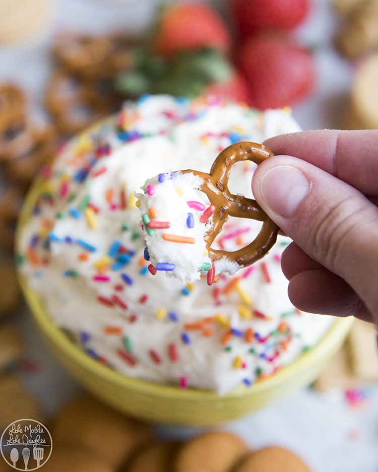 A pretzel dipped into cake batter dip with sprinkles.
