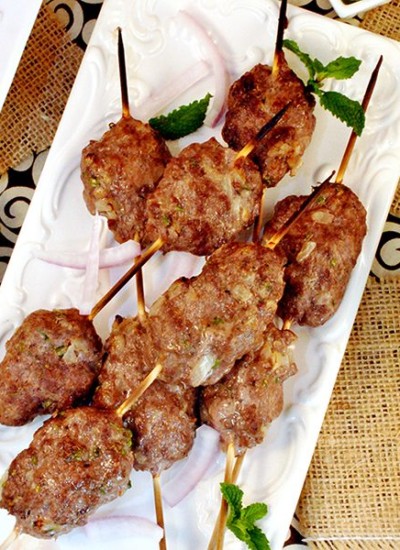 Above view of lamb kebabs on a white square plate.