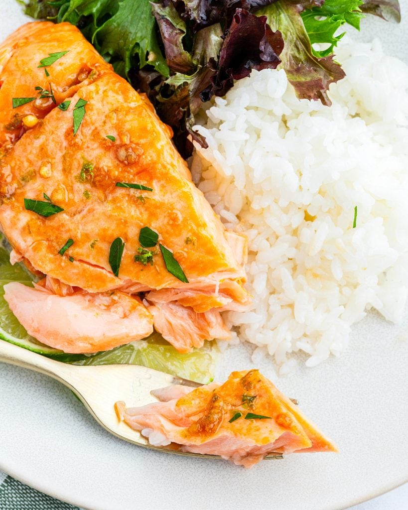 A piece of honey lime salmon on a plate, wit a bite of it on a fork.