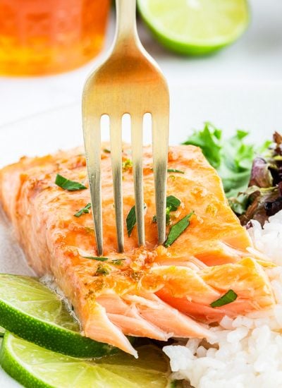 A fork stuck into a salmon fillet on a plate, showing the flakey salmon pieces.