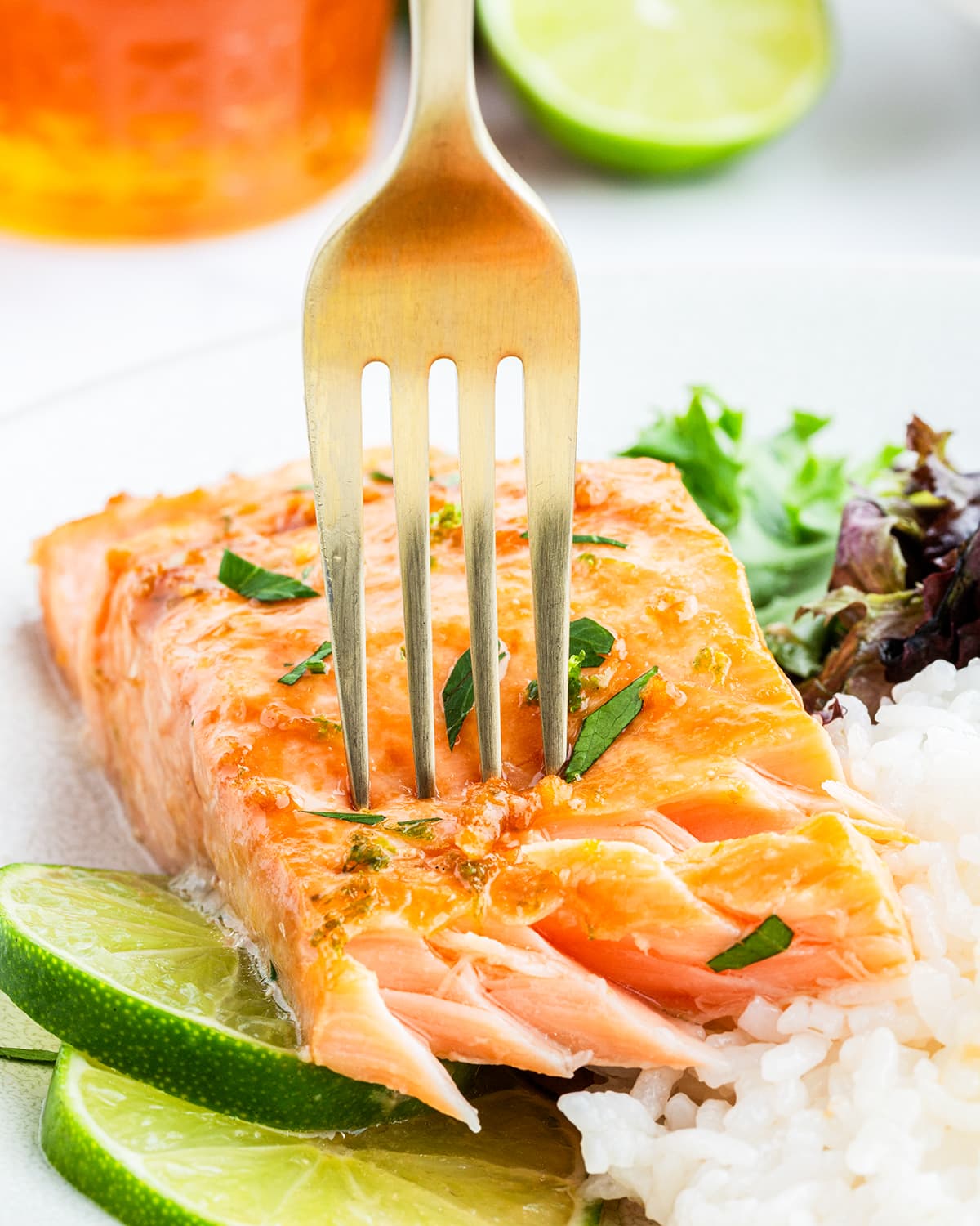 A fork stuck into a salmon fillet on a plate, showing the flakey salmon pieces.