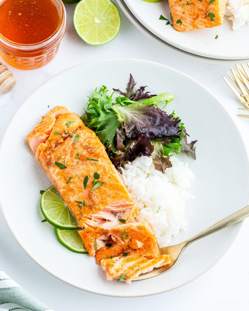 An overhead photo of a salmon fillet on a plate, with white rice, and a green salad.