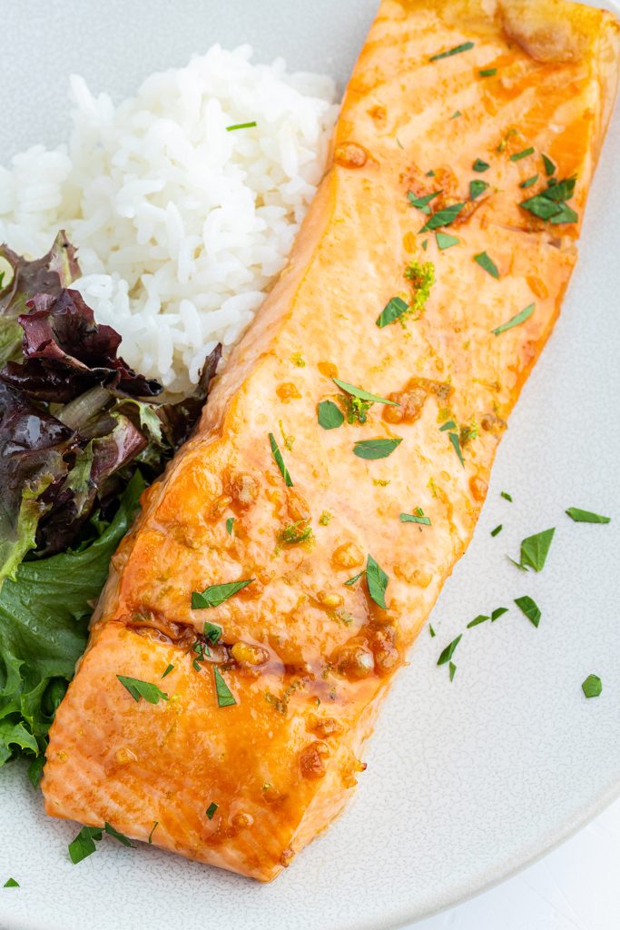 A salmon fillet on a plate topped with honey glaze and cilantro, next to white rice.