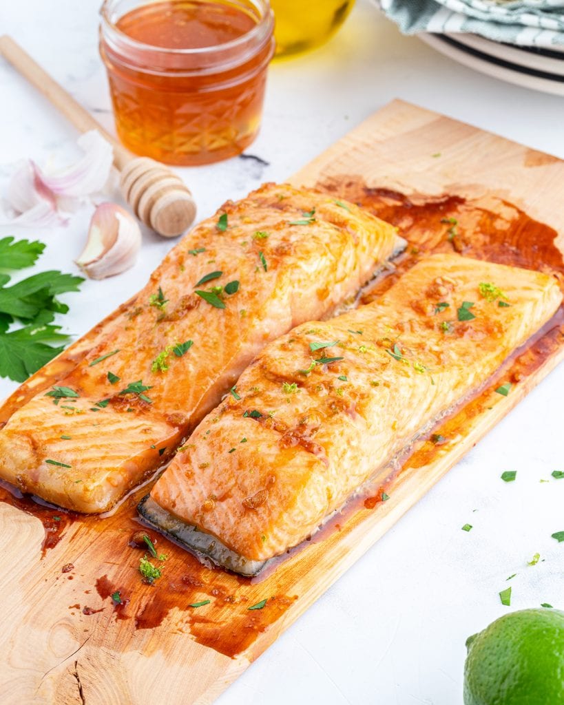 Two cooked salmon fillets on a cedar plank board.