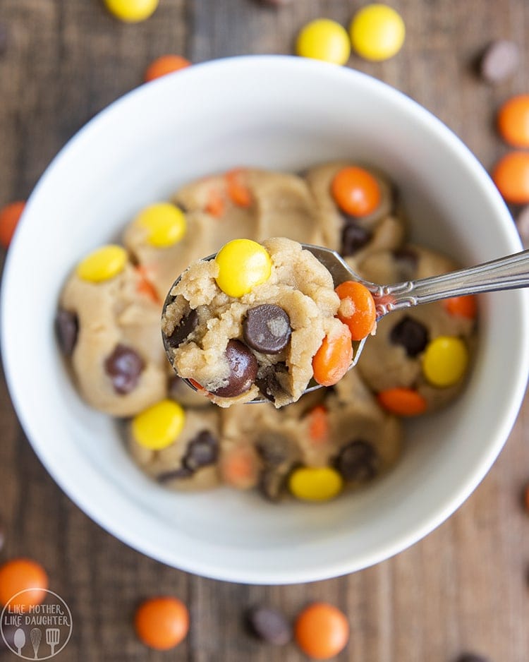 A spoonful of peanut butter cookie dough with reeses pieces and chocolate chips in it.
