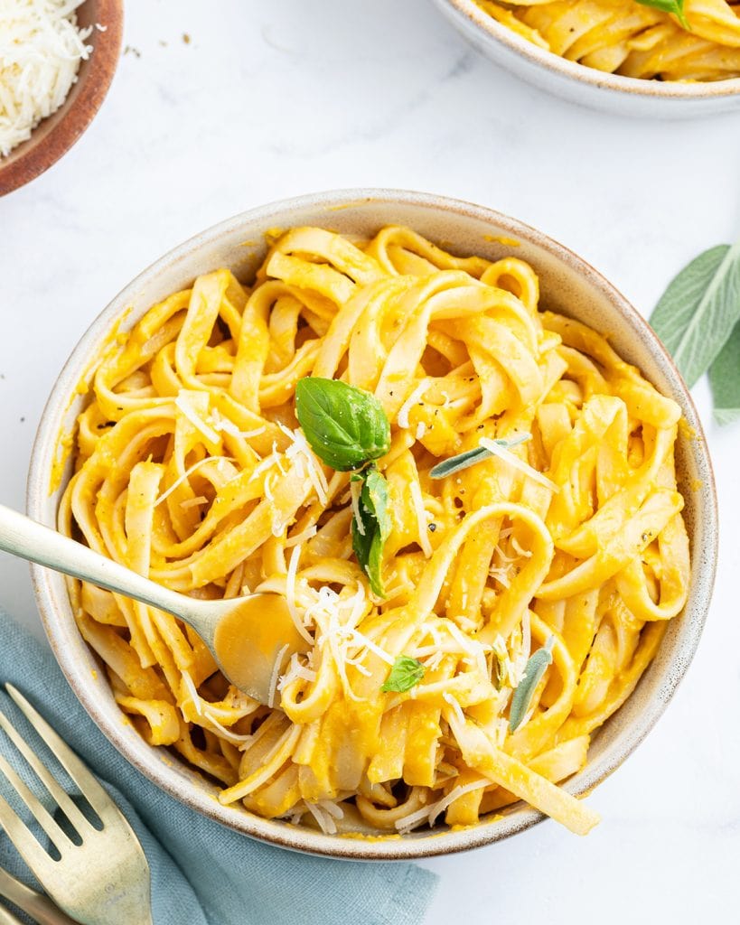 A bowl of butternut squash pasta topped with fresh herbs and parmesan cheese.