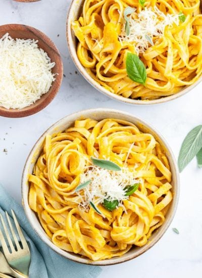 An overhead photo of two bowls of butternut squash pasta, topped with fresh basil and parmesan cheese.