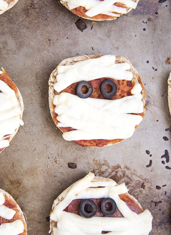 Mummy Mini Pizzas - Delicious and easy mummy pizzas start with an English muffin base, string cheese bandages and olives for eyes and make the perfect Halloween meal! 