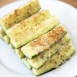 Angled view of parmesan zucchini spears stacked on a white plate.