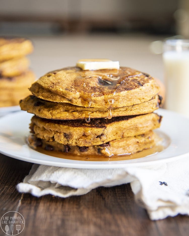 A stack of pumpkin pancakes on a plate with butter and syrup.
